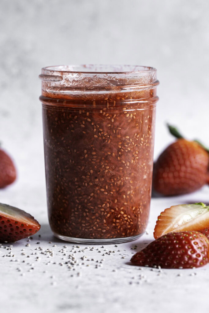 a jar of a jar of strawberry chia seed jam with fresh strawberries around it.