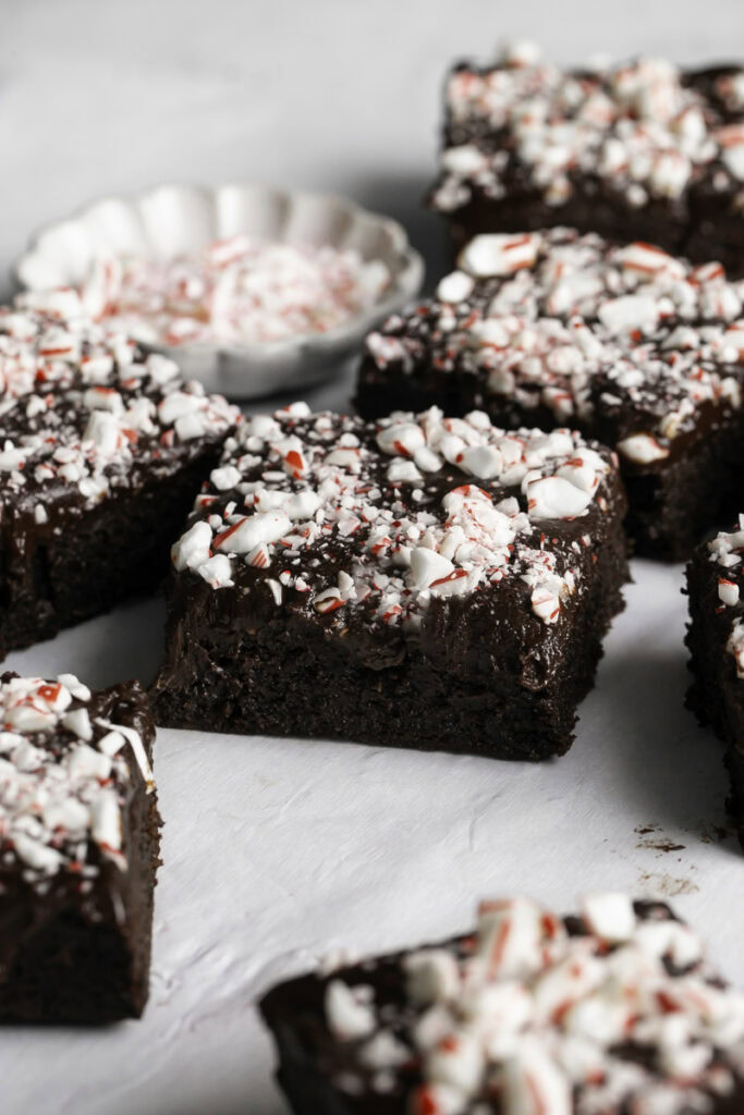 Fudgy Flourless Peppermint Date Brownies cut into squares on a piece of parchment paper with a bowl of crushed candy canes.