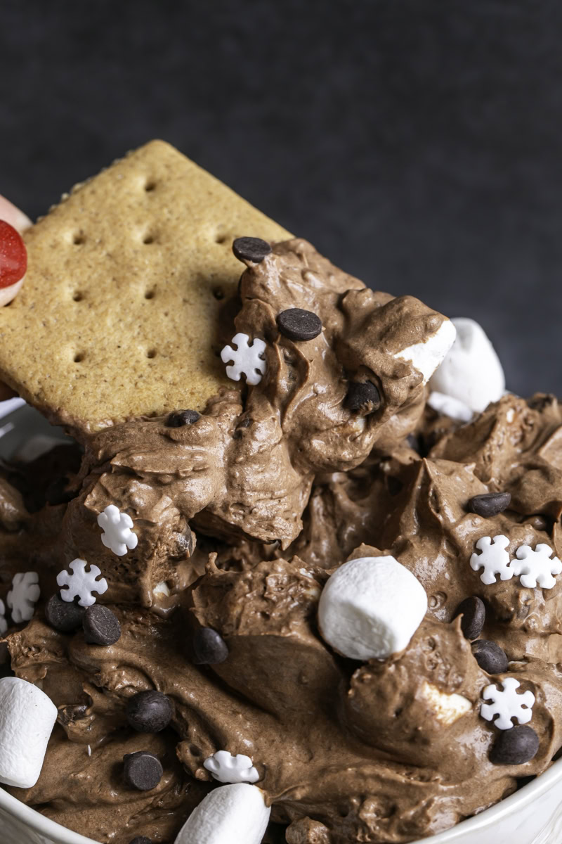 action shot of dipping a graham cracker in the hot cocoa dip.
