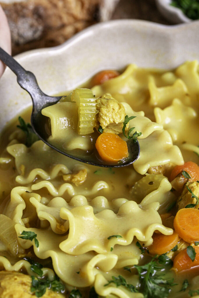 a spoon scooping some vegan lemon turmeric chicken noodle soup out of the bowl.