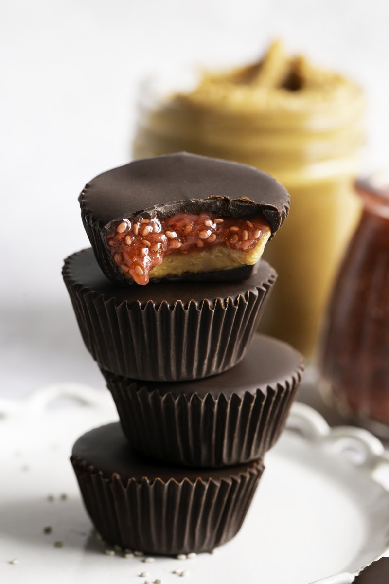 Peanut Butter & Jelly Chocolate Cups stacked on top of one another, the top one with a bite taken out of it to reveal the peanut butter and jelly filling.
