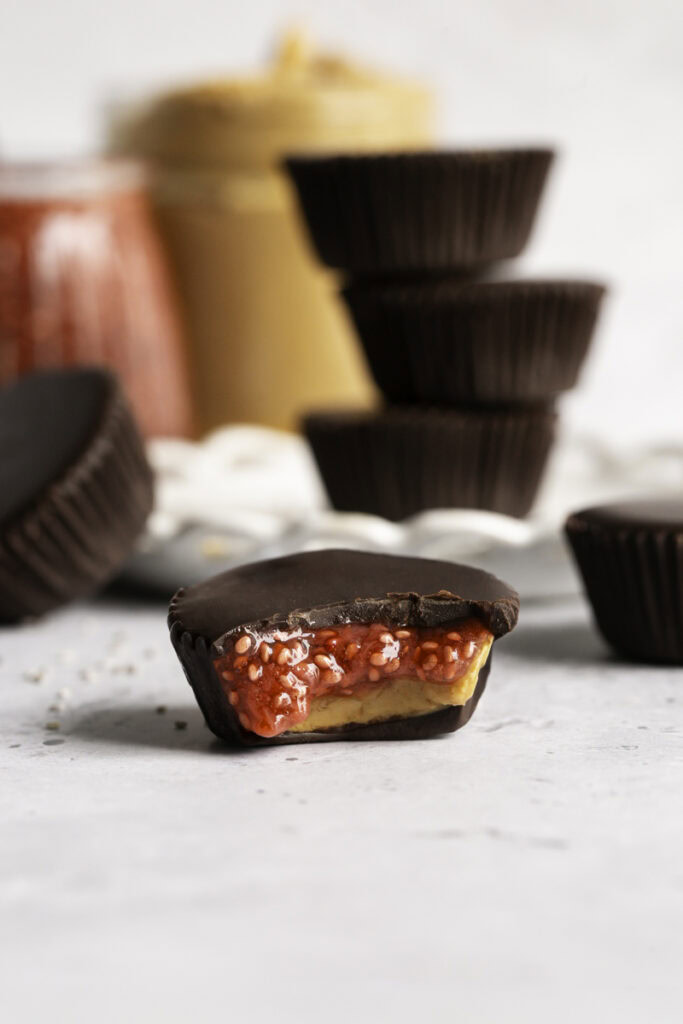 a single peanut butter and jelly chocolate cup with a bite taken out of it to reveal the pb&j filling.