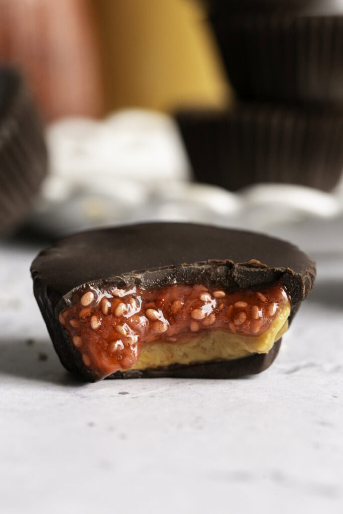 a close up of a single peanut butter and jelly chocolate cup with a bite taken out of it to reveal the pb&j filling.