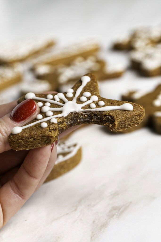 a hand holding a gingerbread cookie with a bite taken out of it to reveal the chewiness of the cookies.
