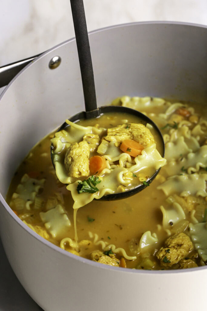 a soup spoon scooping some vegan lemon turmeric chicken noodle soup out of the pot.