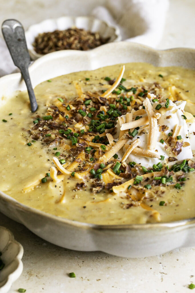 close up macro shot of a bowl of loaded baked potato soup with small bowls of chopped chives and vegan bacon bits.