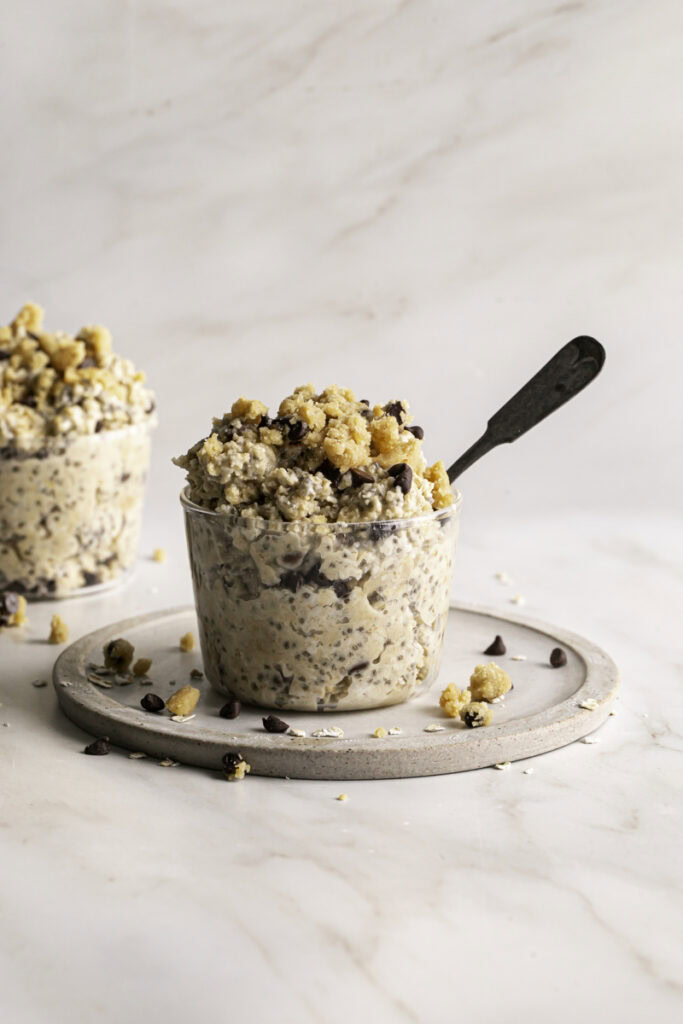 two glasses of chocolate chip cookie dough overnight oats, one with a spoon in it.