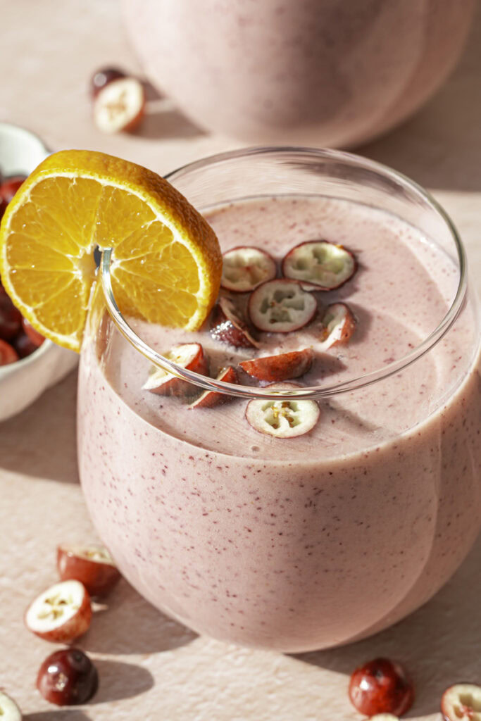 close up of a glass of cranberry clementine smoothie garnished with a clementine slice and fresh cranberries.