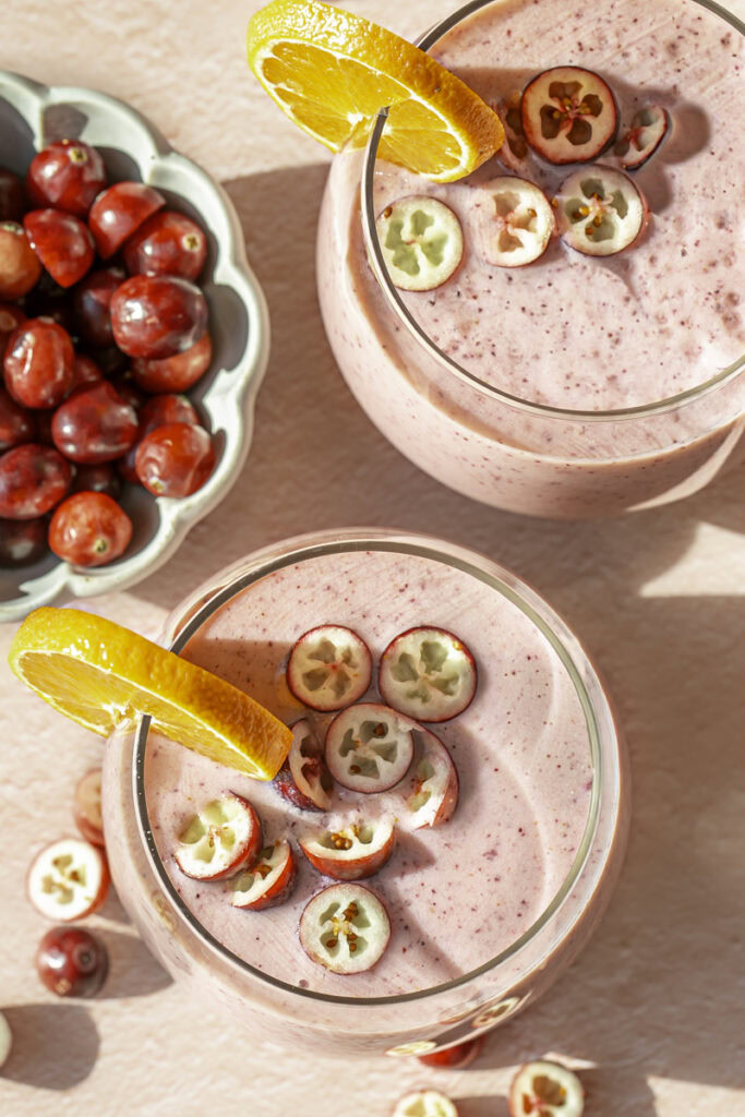 overhead shot of two glasses of cranberry clementine smoothie with a bowl of fresh, whole cranberries.