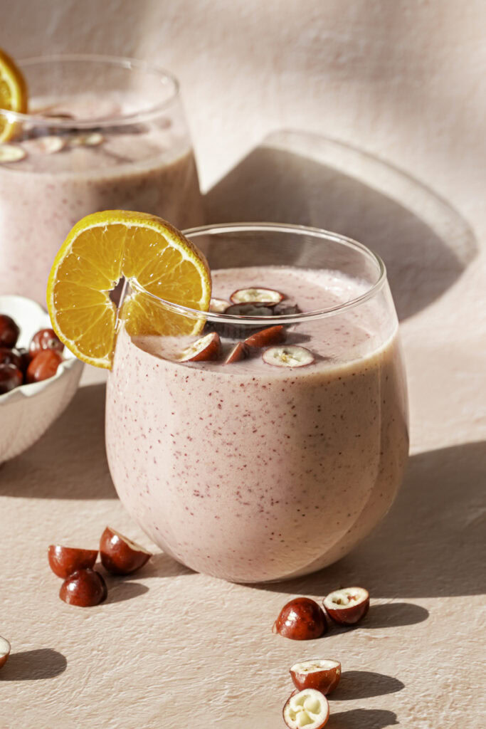 two glasses of cranberry clementine smoothie garnished with a clementine slice and fresh cranberries.