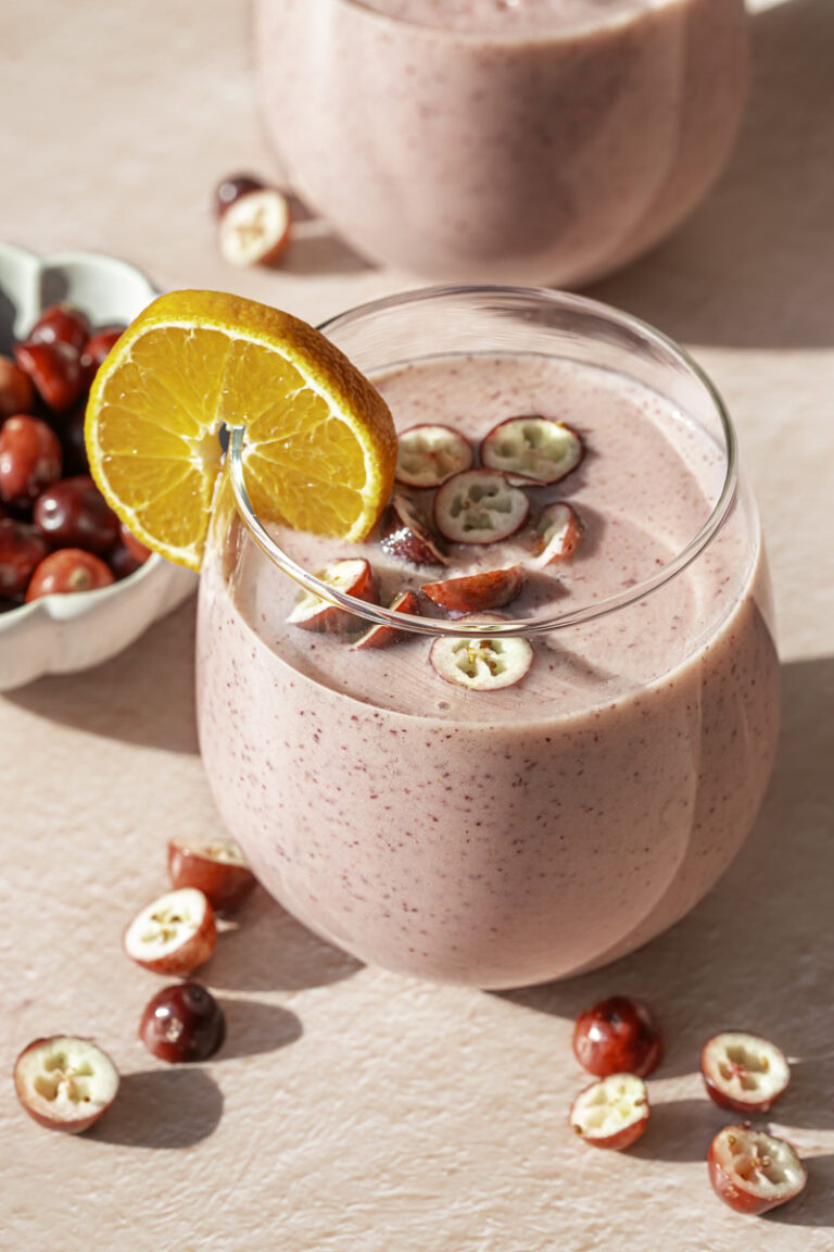 two glasses of cranberry clementine smoothie garnished with a clementine slice and fresh cranberries.