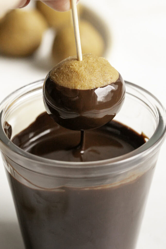 action shot of dipping the peanut butter buckeye in melted chocolate.