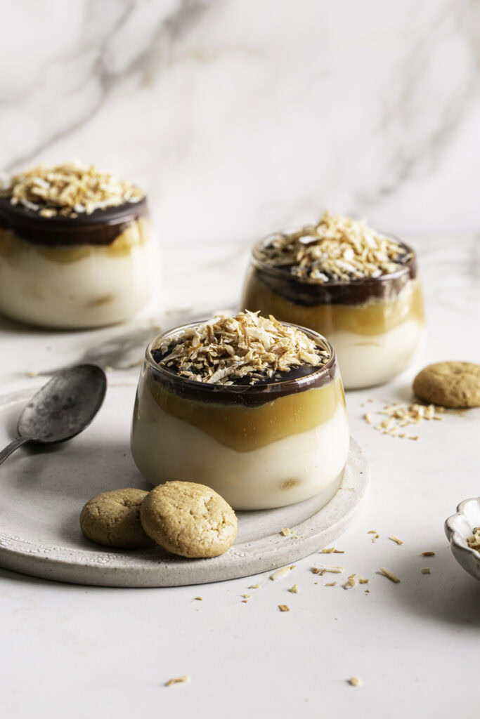 three glasses of Samoas Yogurt Dessert Cups with shredded toasted coconut and mini vanilla cookies.