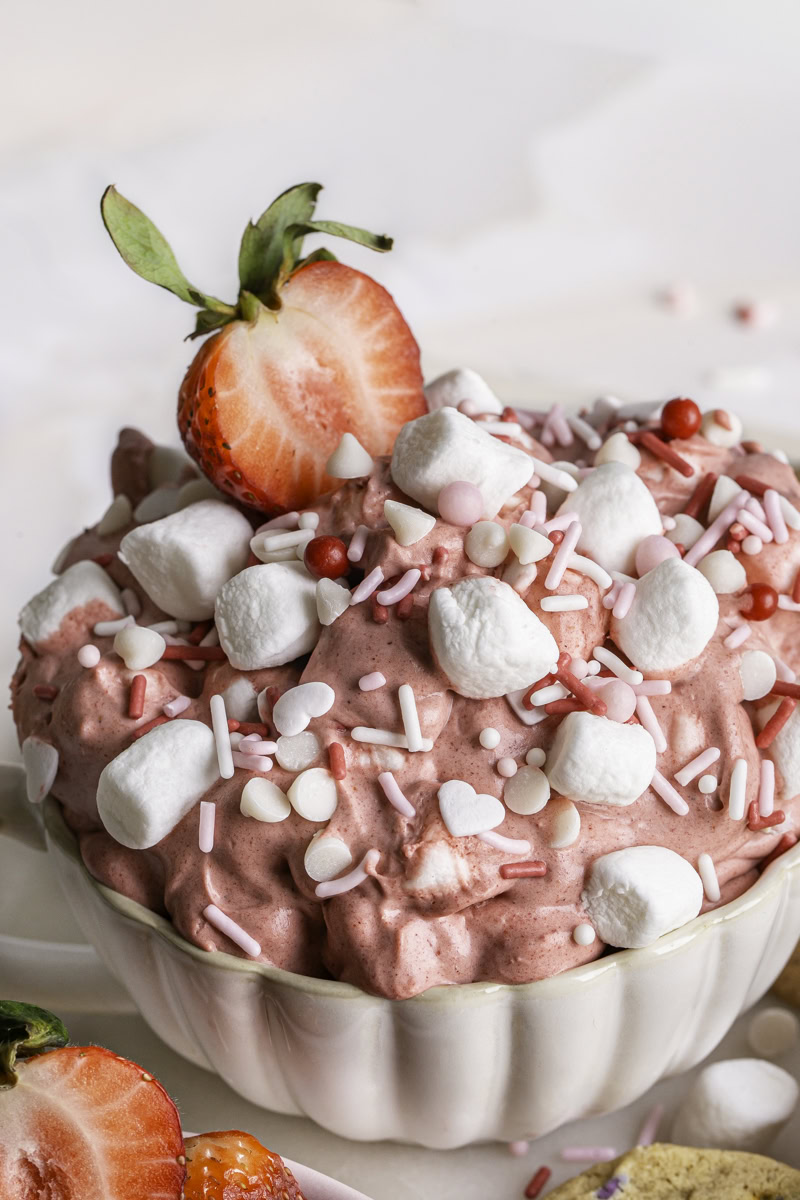 a close up of Creamy Strawberry White Chocolate Marshmallow Dip in a mug with a strawberry sticking out of the dip.