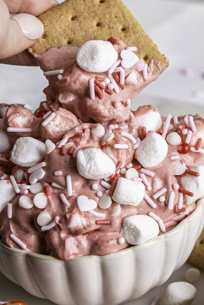 action shot of a graham cracker being dipped in the Strawberry White Chocolate Coconut Milk Marshmallow Dip.
