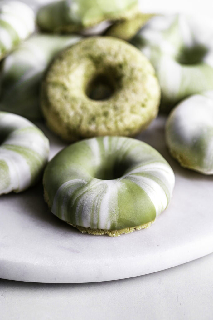 close up of No-Bake Protein Matcha Donuts piled on top of one another on a round marble plate.
