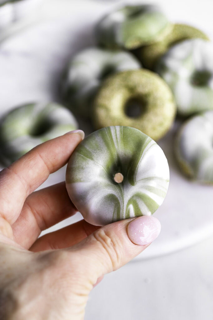 a hand holding a mini matcha donut with the other donuts in the background.