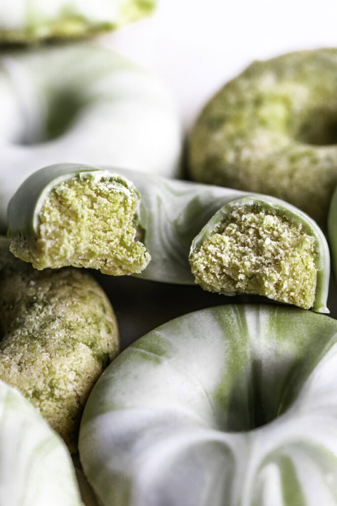 a close up of No-Bake Protein Matcha Donuts, the top one with a bite taken out of it to reveal the donut texture.