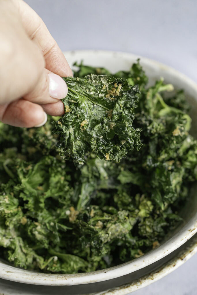 a hand picking out a kale chip from the bowl.