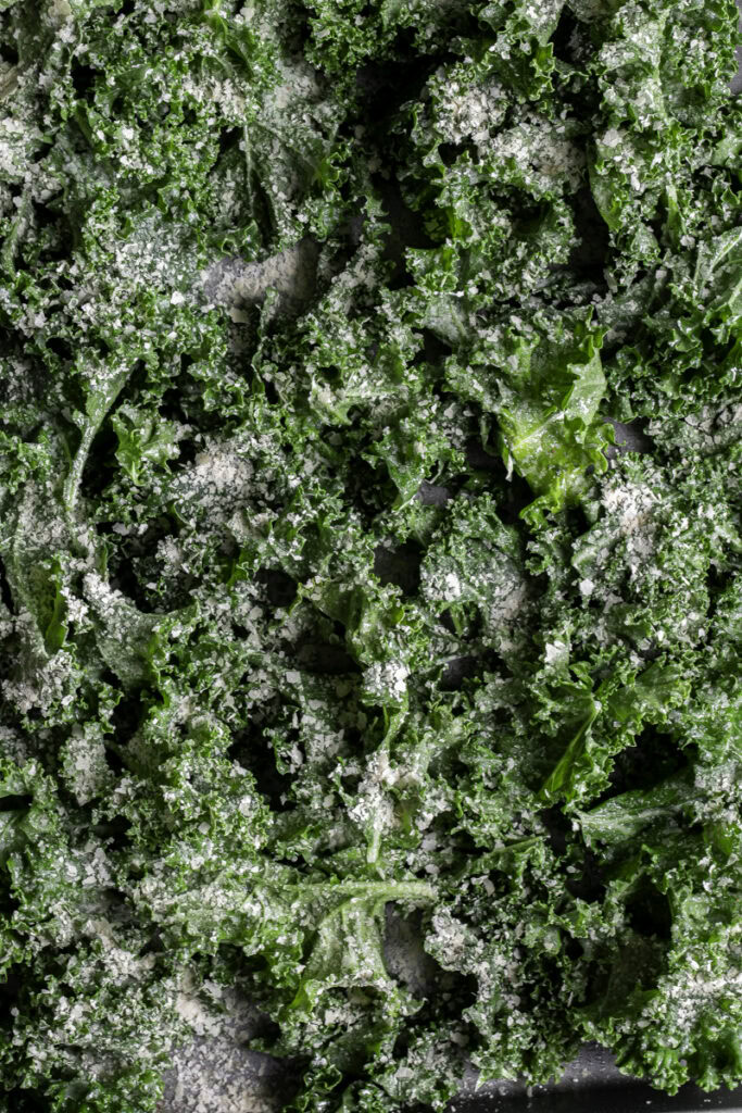 raw kale on a baking sheet sprinkled with nutritional yeast and salt.