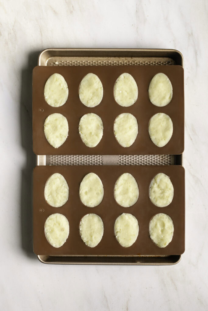 two egg molds filled with mashed potatoes on a baking sheet ready to be baked in the oven.
