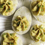 a plate of deviled mashed potato eggs garnished with chopped chives and smoked paprika.