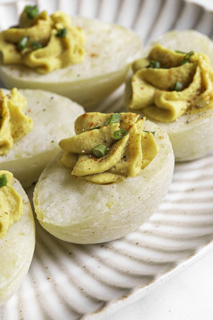 a plate of deviled mashed potato eggs garnished with chopped chives and smoked paprika.