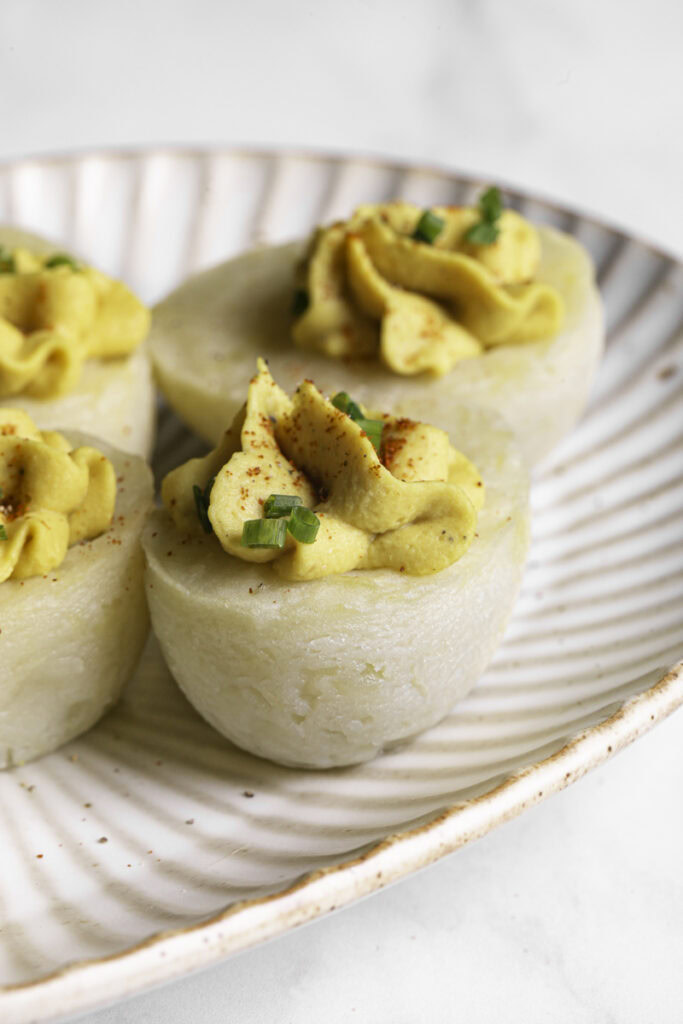 a close up of a couple of deviled mashed potato eggs garnished with chopped chives and smoked paprika on a plate.
