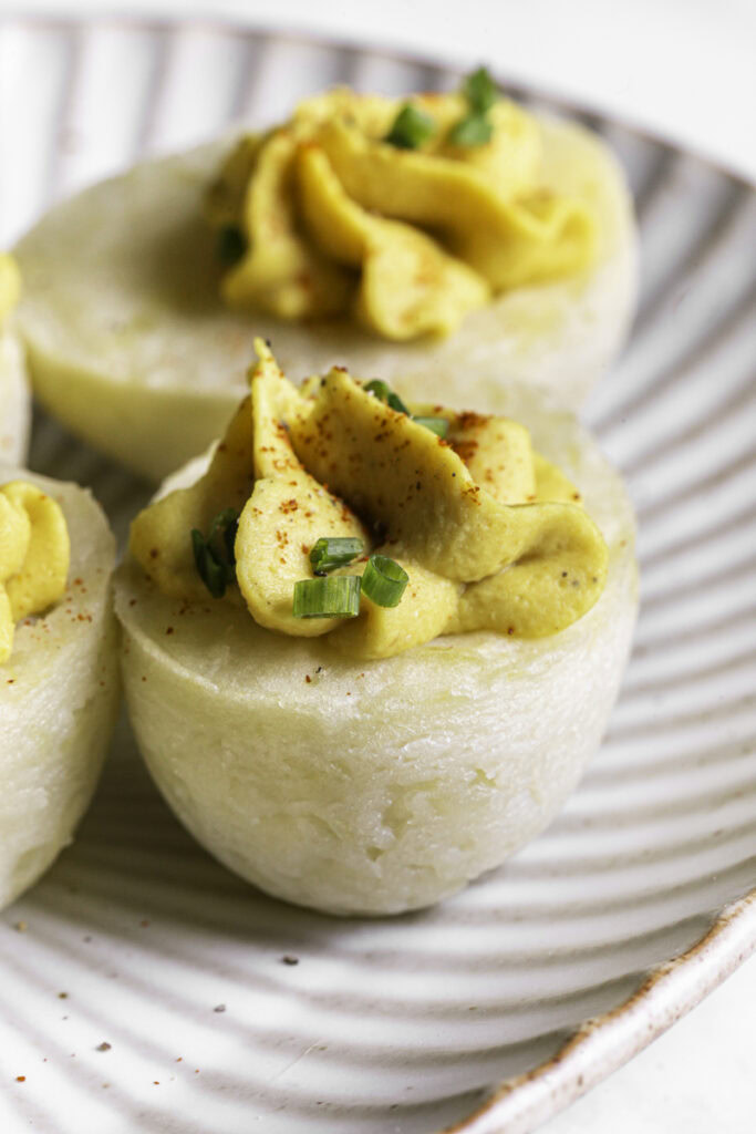 a close up of a couple of deviled mashed potato eggs garnished with chopped chives and smoked paprika on a plate.