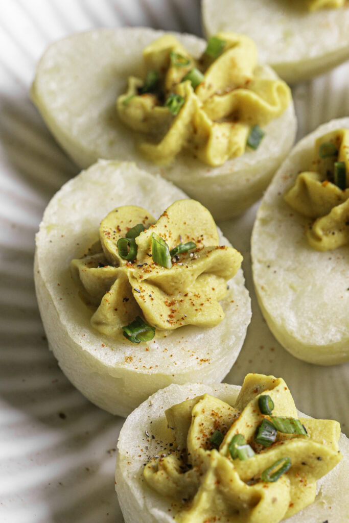 a close up of a couple of deviled mashed potato eggs garnished with chopped chives and smoked paprika on a plate.