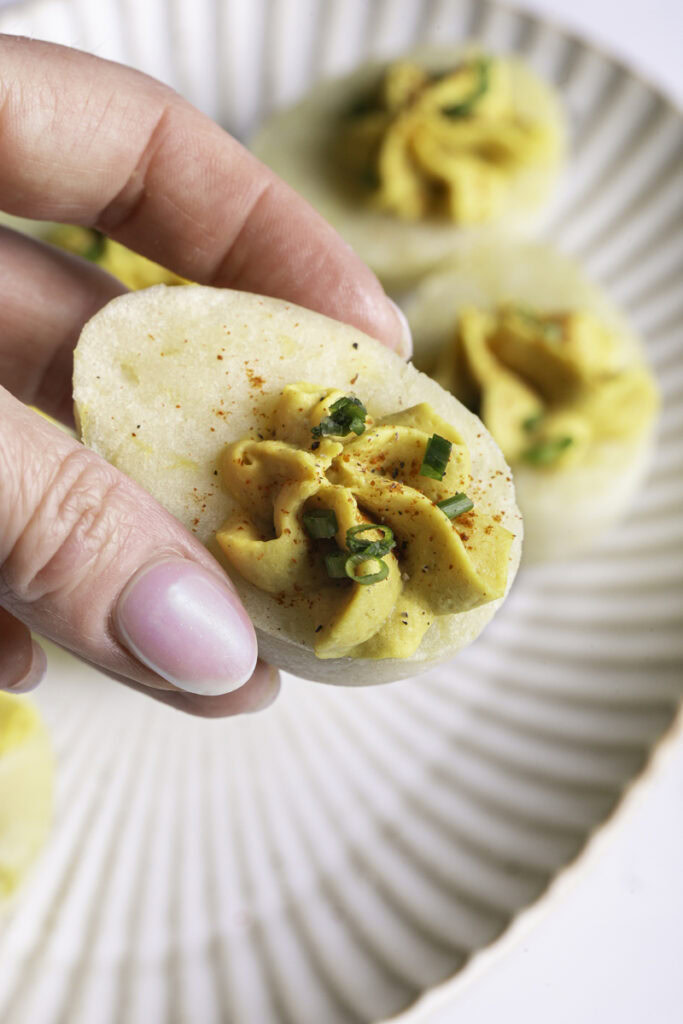 a hand holding a mashed potato deviled "egg".