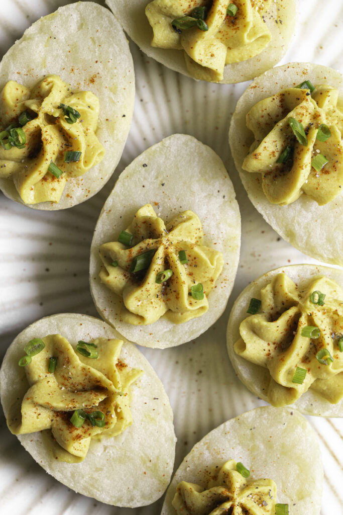 a plate of deviled mashed potato eggs garnished with chopped chives and smoked paprika.