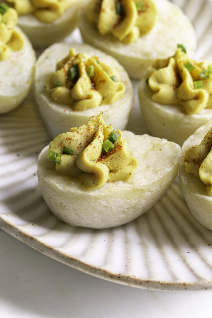 a close up of a couple of deviled mashed potato eggs garnished with chopped chives and smoked paprika on a plate.