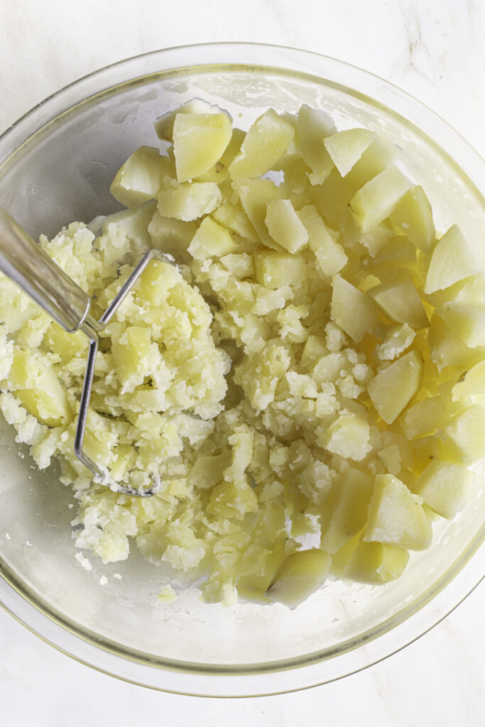 action shot of mashing potatoes in a glass bowl with a potato masher.