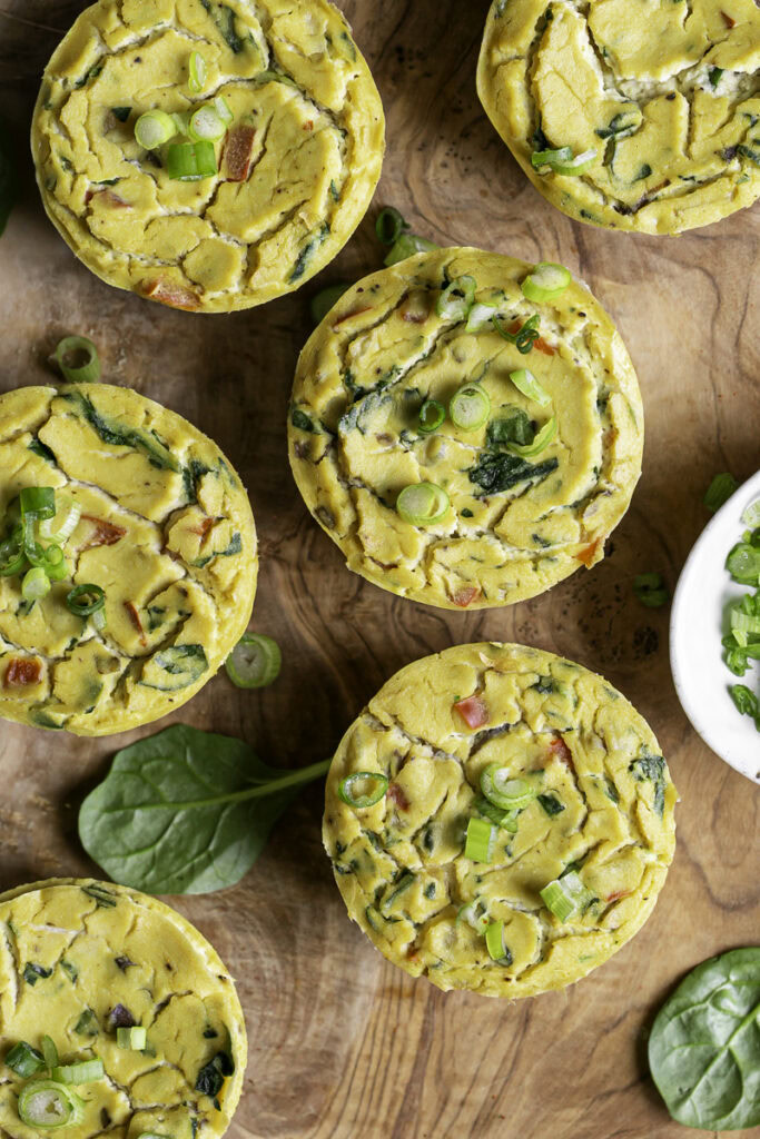 overhead shot of vegan baked spinach mushroom pepper onion egg bites on a wooden cutting board.