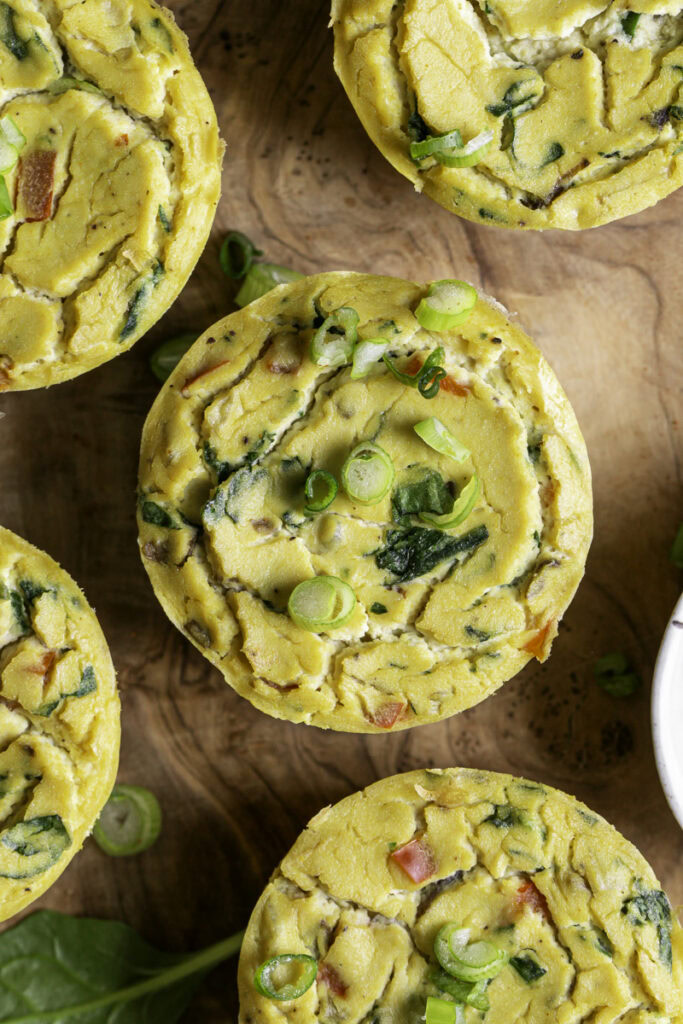 close up overhead shot of vegan baked spinach mushroom pepper onion egg bites on a wooden cutting board.