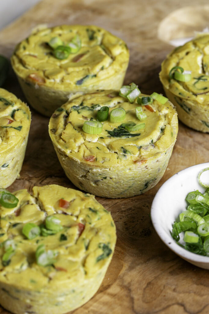 3/4 shot of vegan baked spinach mushroom pepper onion egg bites on a wooden cutting board with a small bowl of sliced green onion.
