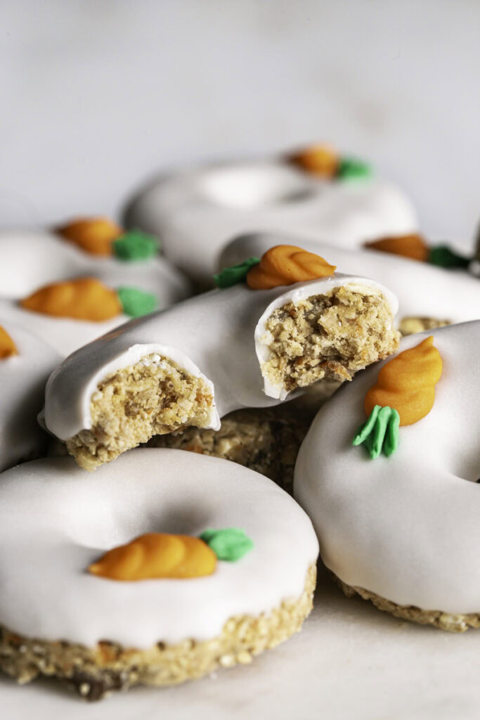 a close up of no-bake carrot cake protein mini donuts stacked on top of one another, the top one cut in half to reveal the donut texture.
