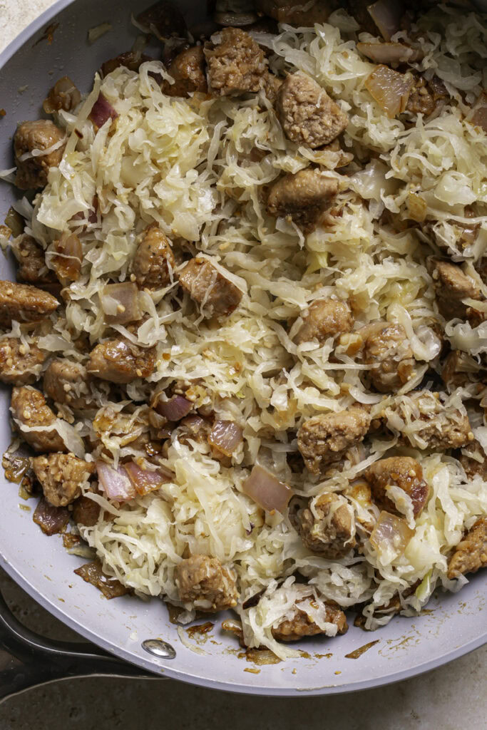 sauerkraut added to the skillet with the cooked bratwurst and onion.