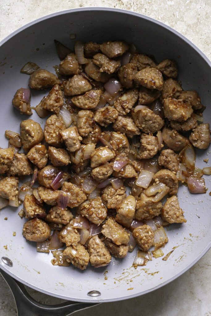plant-based bratwurst, red onion, and minced garlic cooked in a skillet.