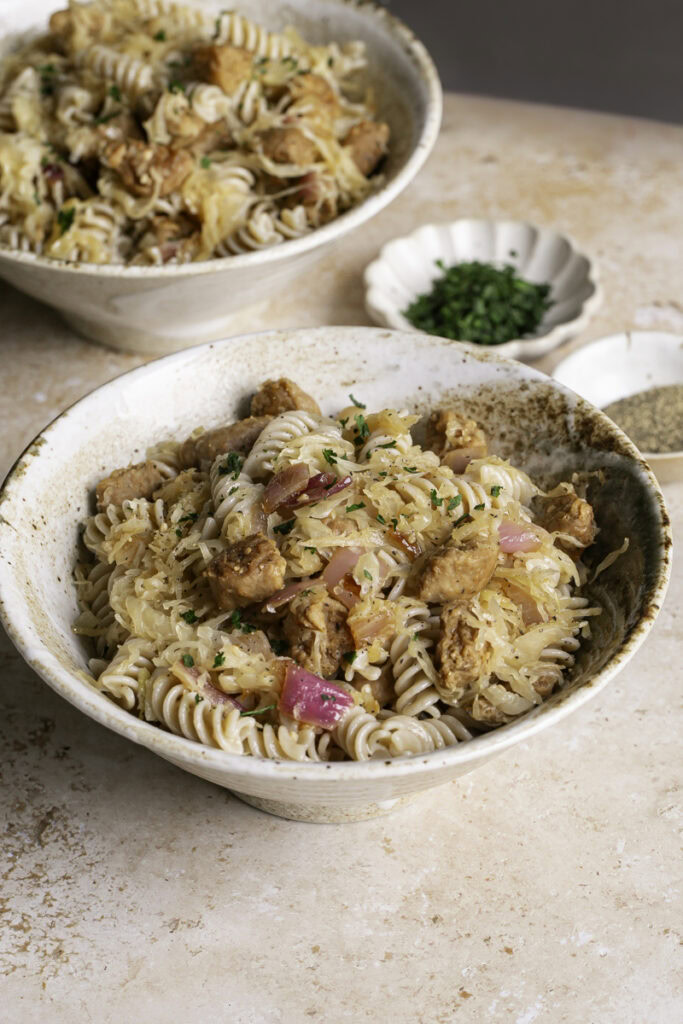 3/4 image of vegan bratwurst and sauerkraut pasta served into bowls.