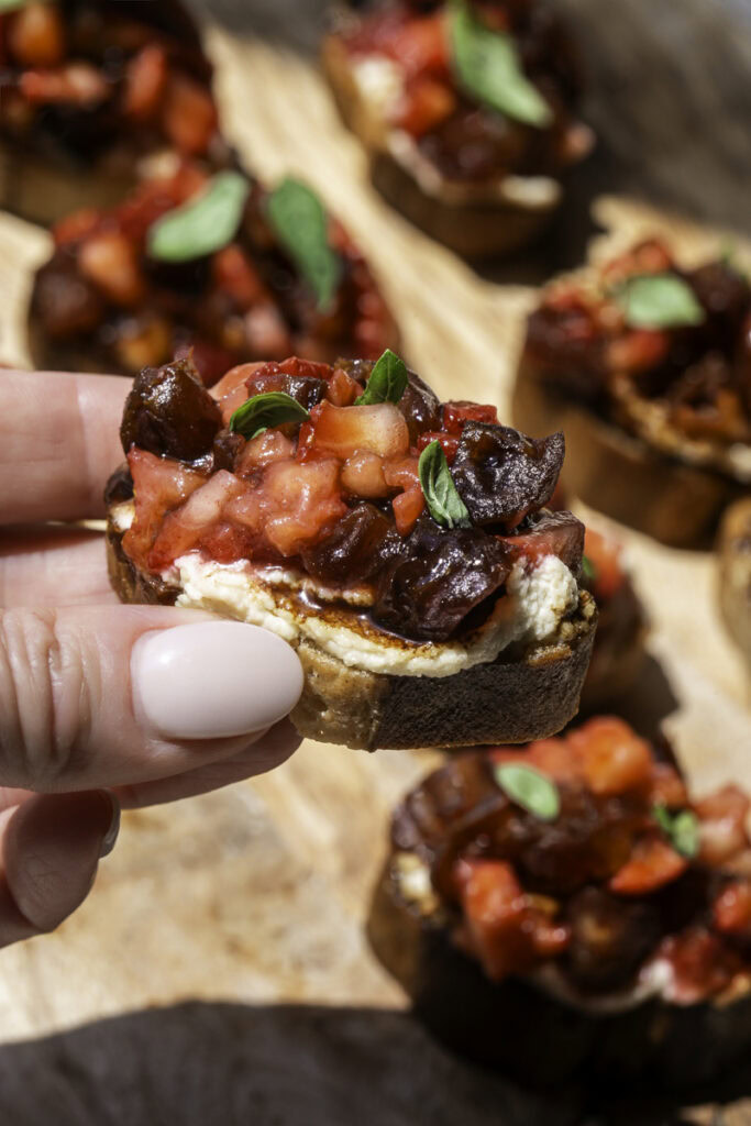 a hand holding a crostini with more crostini in the background on a wooden board.