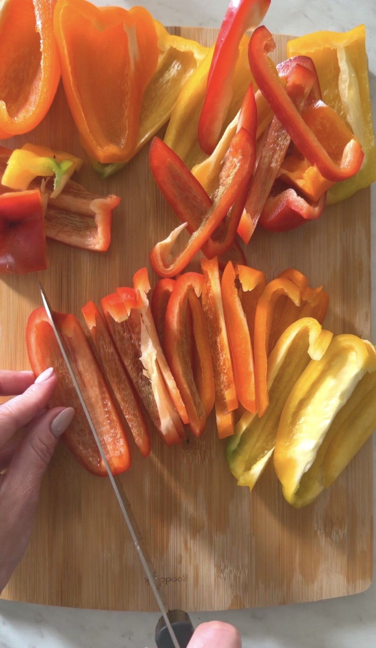 action shot slicing bell peppers on a wooden cutting board.