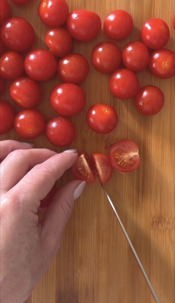 action shot slicing cherry tomatoes on a wooden cutting board.