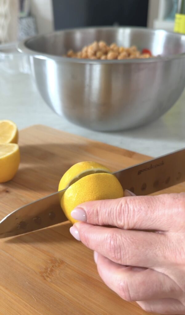action shot slicing a lemon in half on a wooden cutting board.