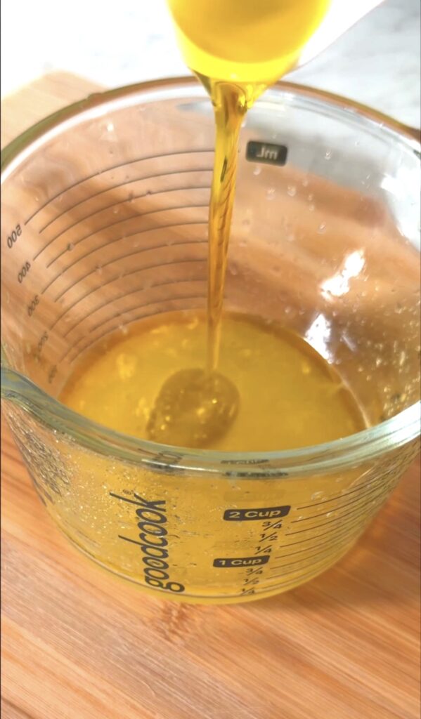 pouring olive oil into the measuring cup with the lemon juice.