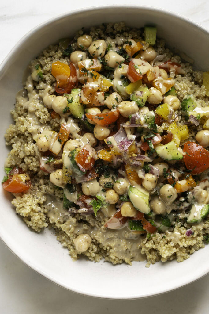 chickpea salad served over a bowl of quinoa with a drizzle of tahini.