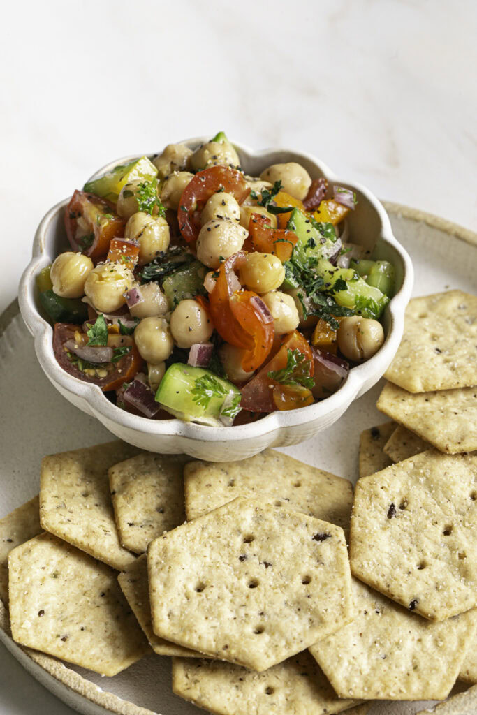 chickpea salad in a small bowl on a plate with some crackers.