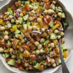 a bowl of chickpea salad with a serving spoon and a small bowl of chopped parsley above it.