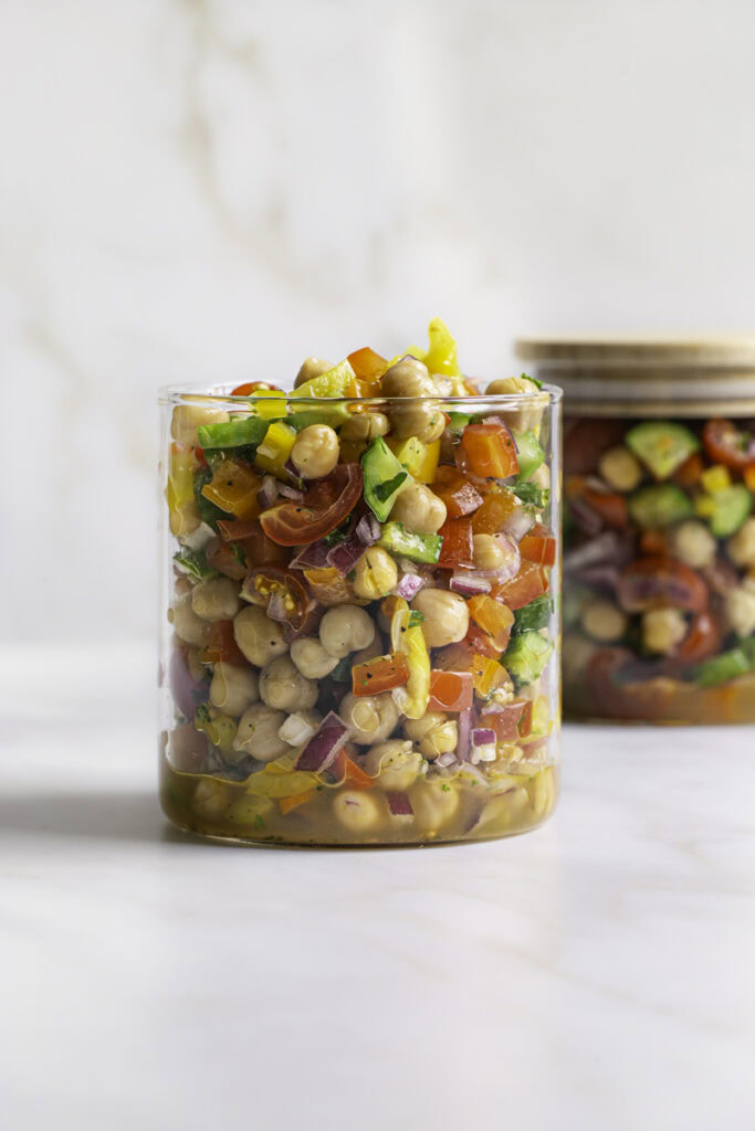 chickpea salad in a glass canister with the lid off and another glass canister filled with salad behind it with the lid on it.